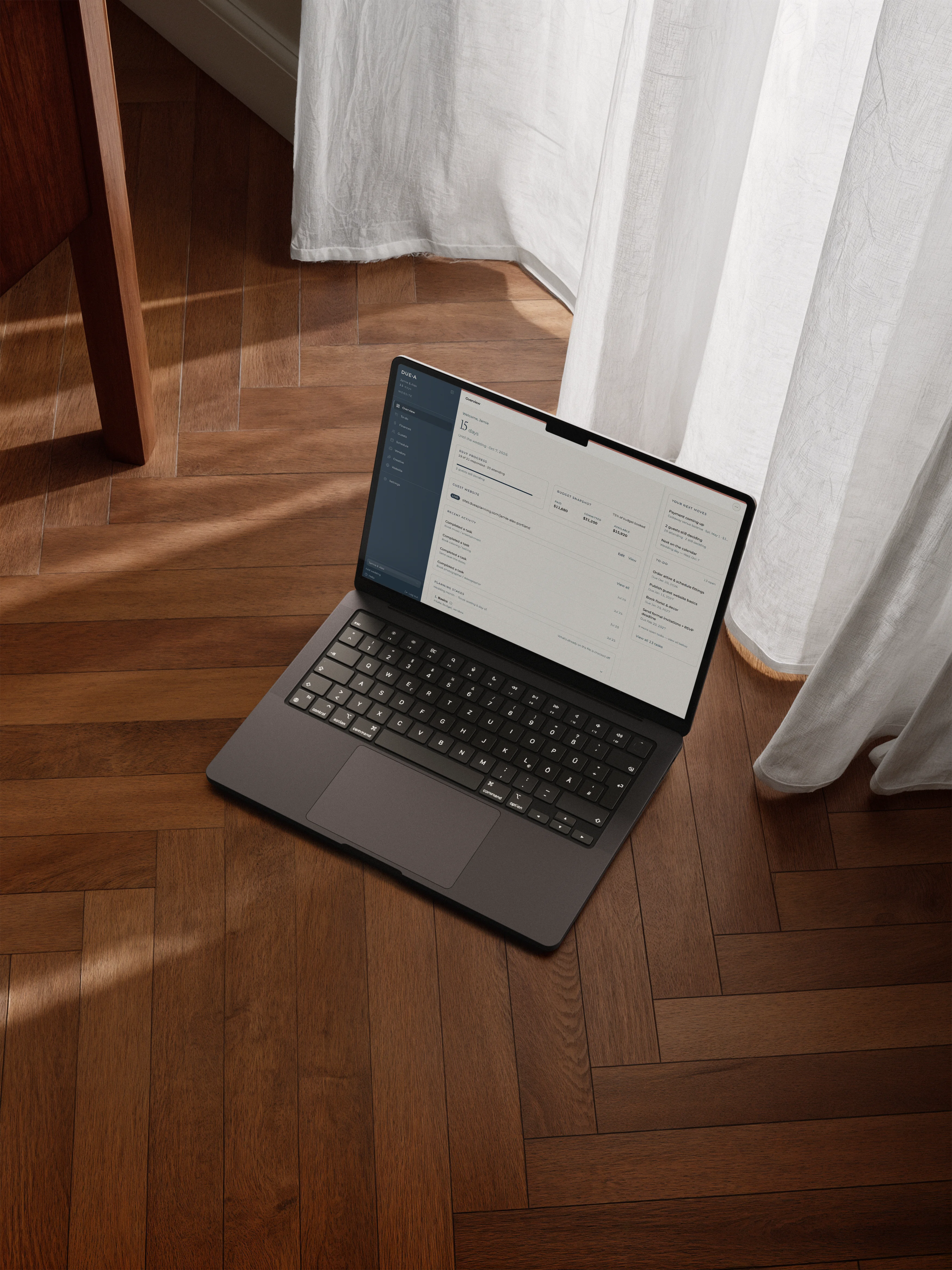 Laptop open to Duea on a wood floor, beside a linen curtain in warm daylight